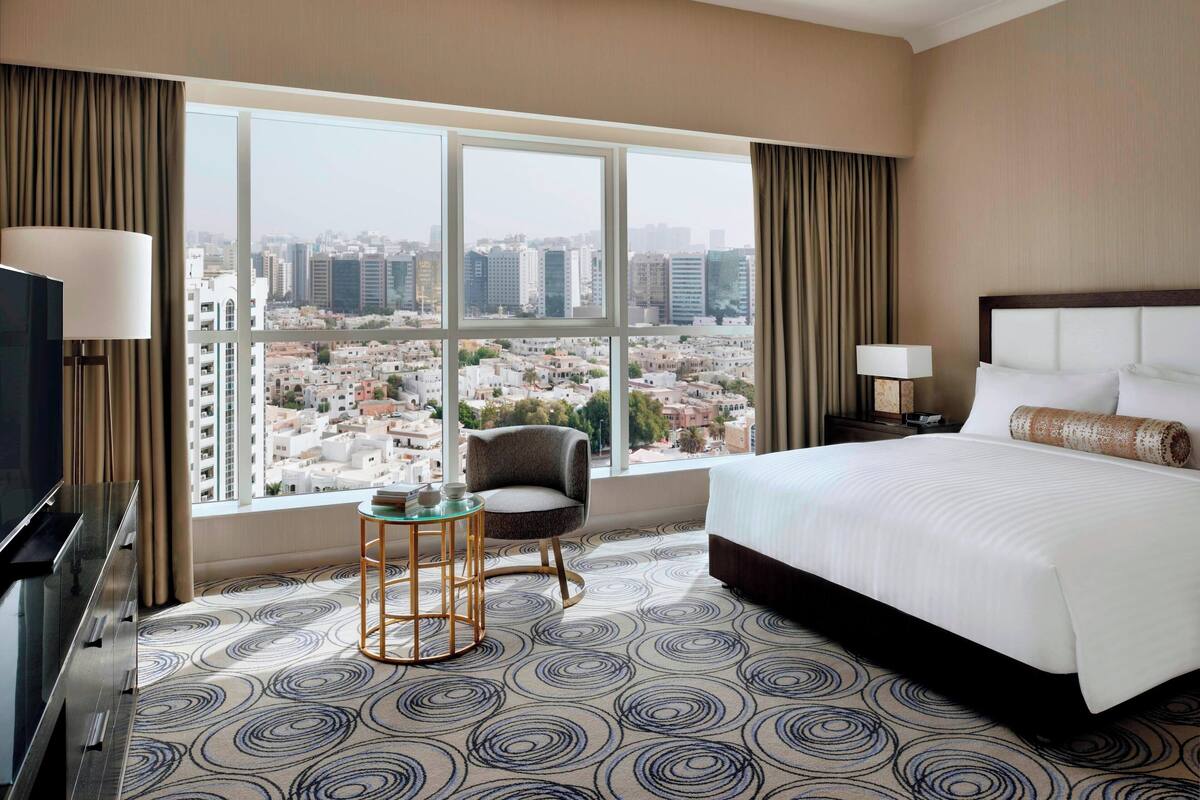 Una habitación de hotel con una cama grande, televisión, una silla y una mesita.