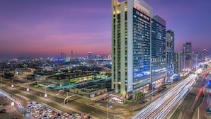 A high-rise hotel with multiple floors, a prominent entrance, and a view of the cityscape in the background.