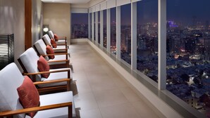A modern hotel room with a balcony overlooking a cityscape at night.