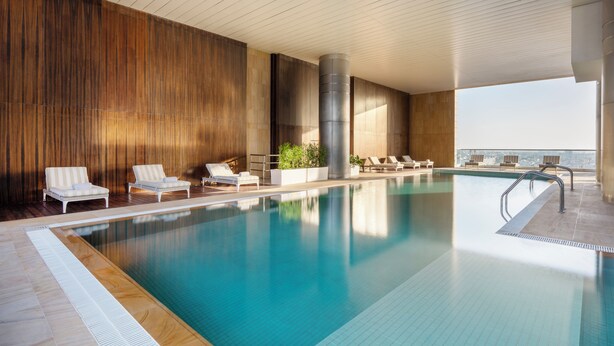 An indoor swimming pool with lounge chairs and a view of the city.