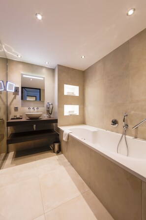 A modern bathroom with a large bathtub, a vanity with a sink, and a mirror. - Van Der Valk Hotel Oostzaan - Amsterdam (Oostzaan)