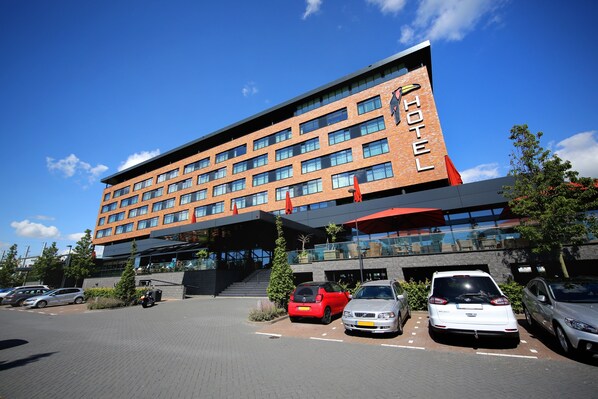 A hotel with a modern brick facade, multiple windows, and a parking lot with several cars. - Van Der Valk Hotel Oostzaan - Amsterdam (Oostzaan)
