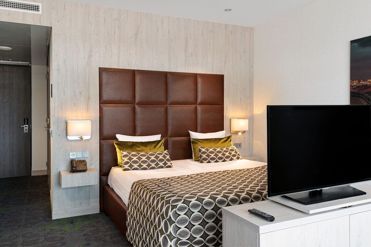 A hotel room with a large bed, a flat-screen TV, a bedside table with a lamp, and a wall-mounted phone.