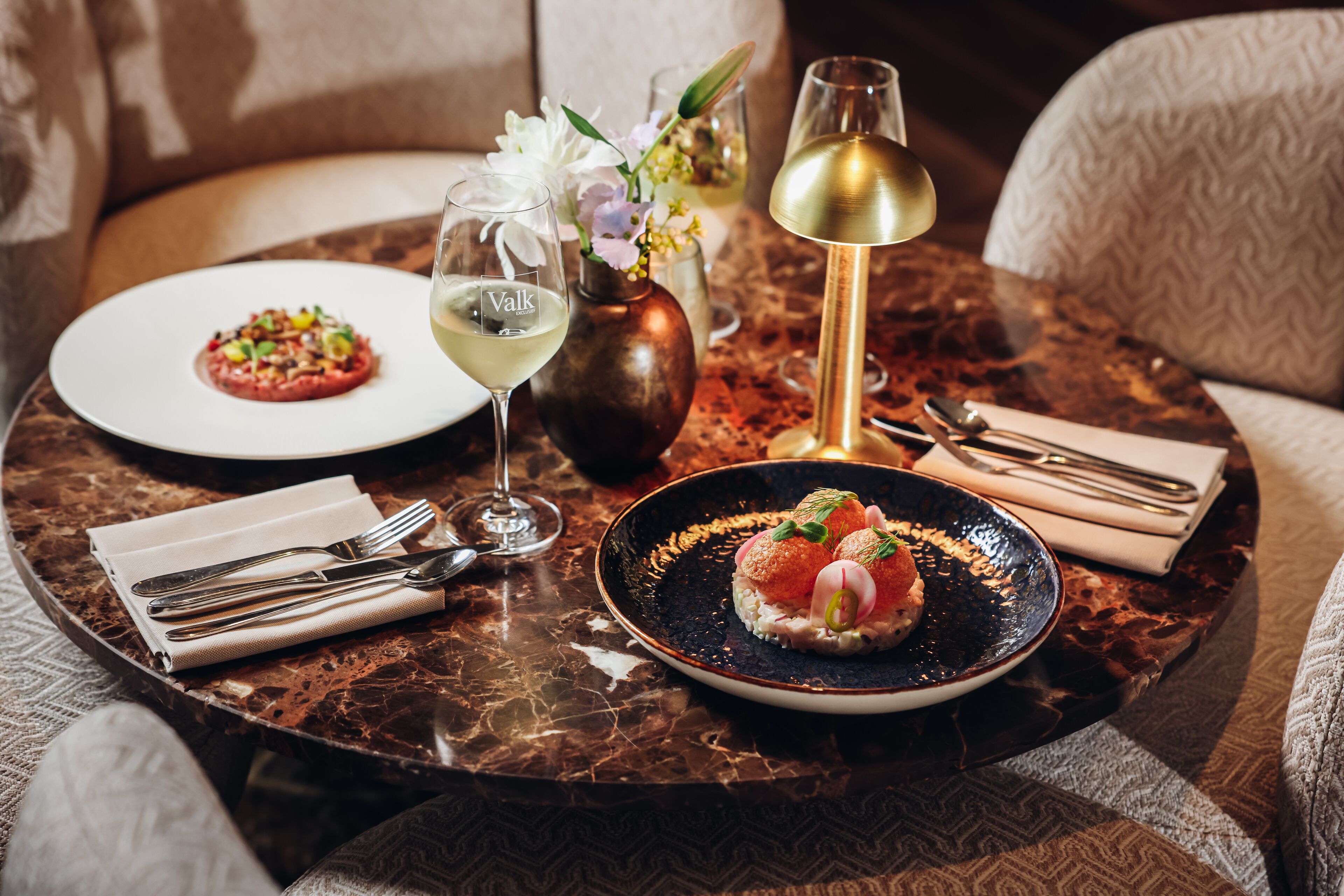 Une table à manger dressée avec une variété d’assiettes, de verres et de couverts, dans une pièce élégamment aménagée.