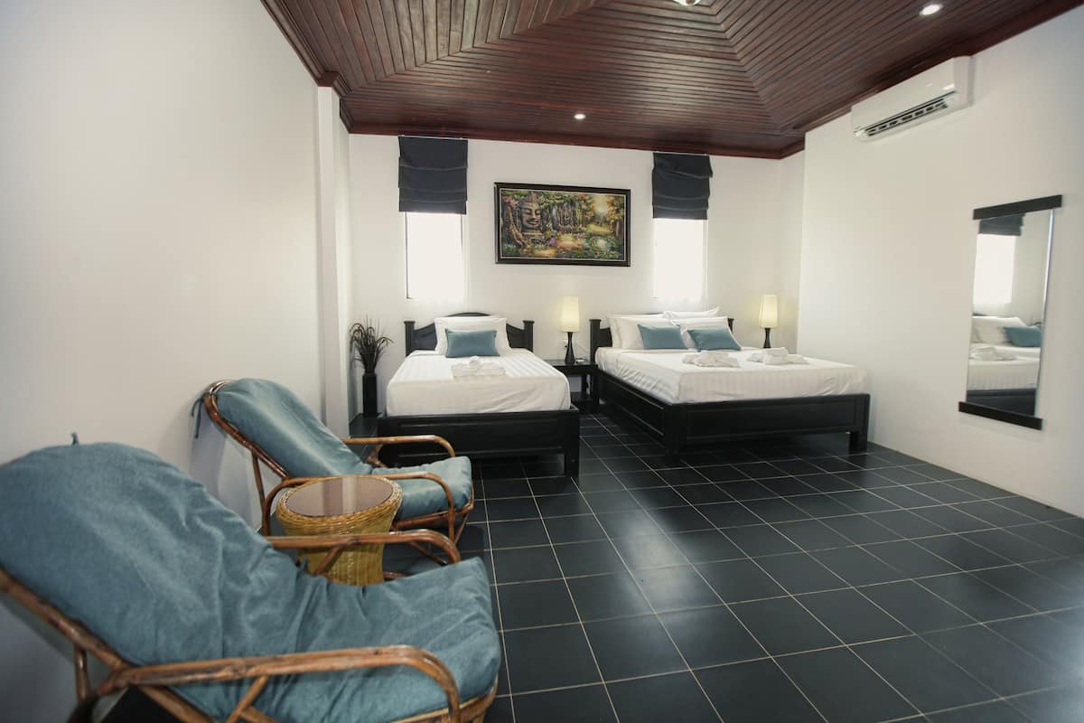 Habitación de hotel con dos camas, una silla de mimbre, un espejo grande y un techo con diseño de madera.