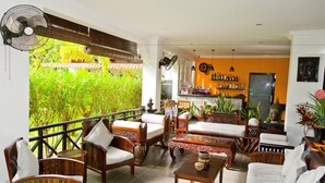 A cozy indoor seating area with wooden furniture, a dining table, and a view of lush greenery outside. - SR Sofia Villa Hotel (Siem Reap)