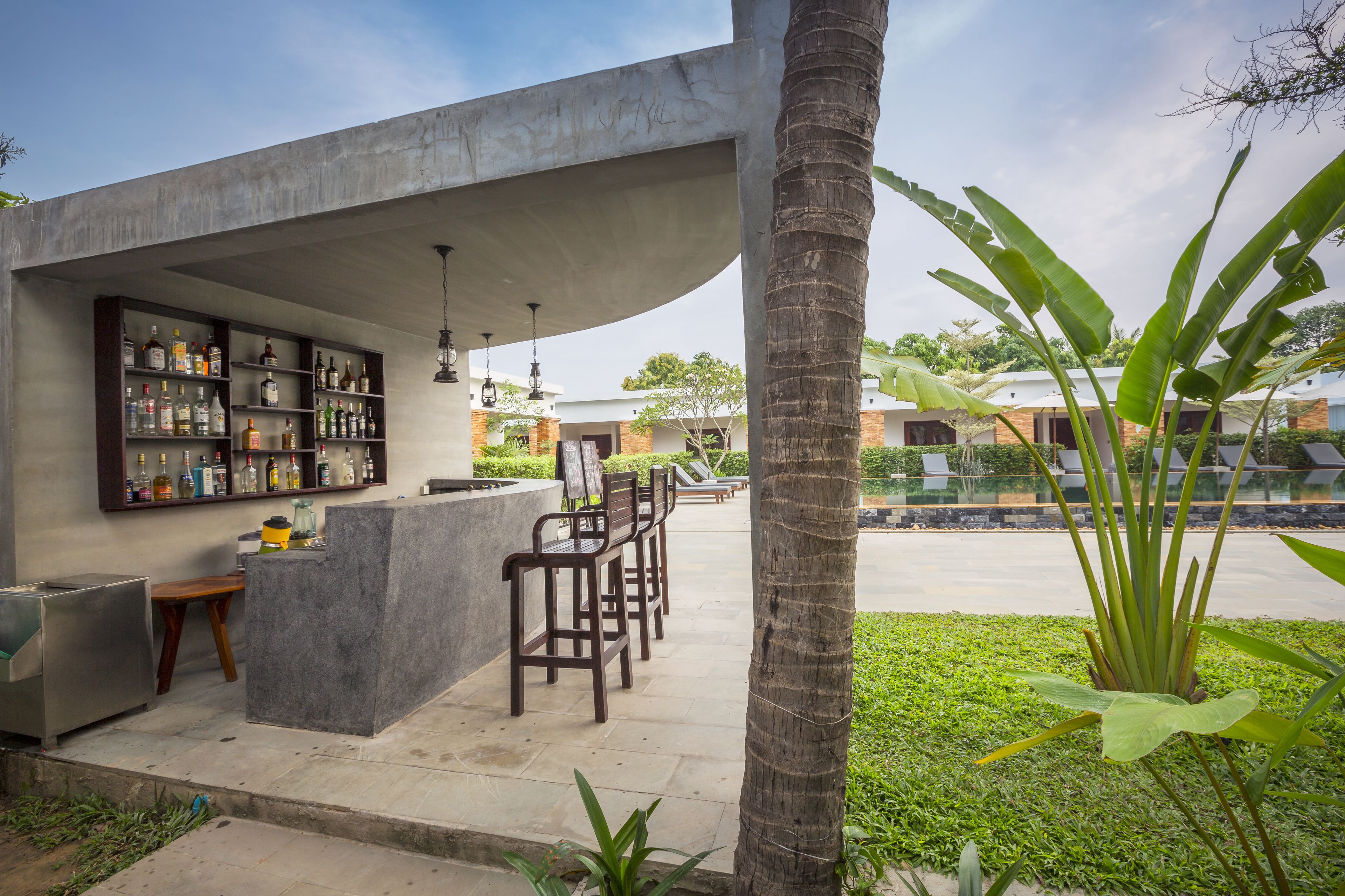 Zona de bar al aire libre con barra de concreto, sillas de madera y una variedad de botellas.