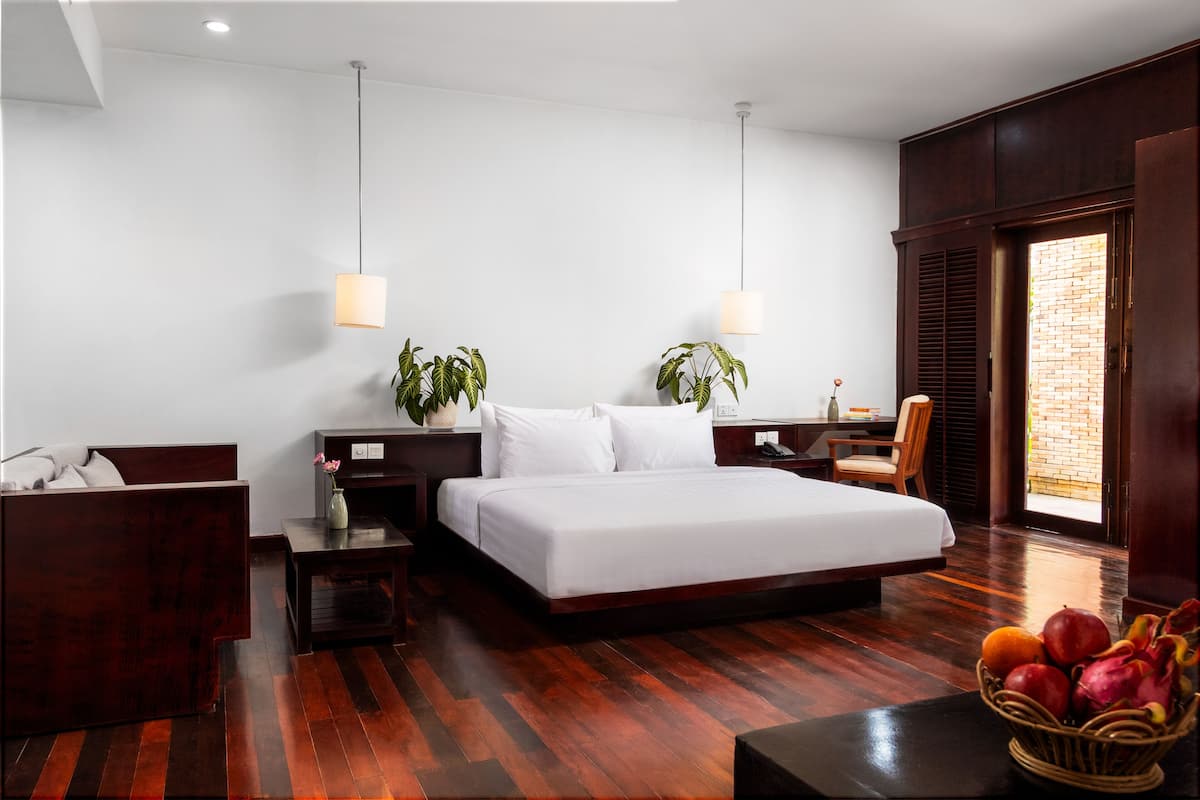Une chambre d’hôtel moderne avec un grand lit, deux tables de chevet, un bureau, une chaise et une fenêtre donnant sur un mur de briques.