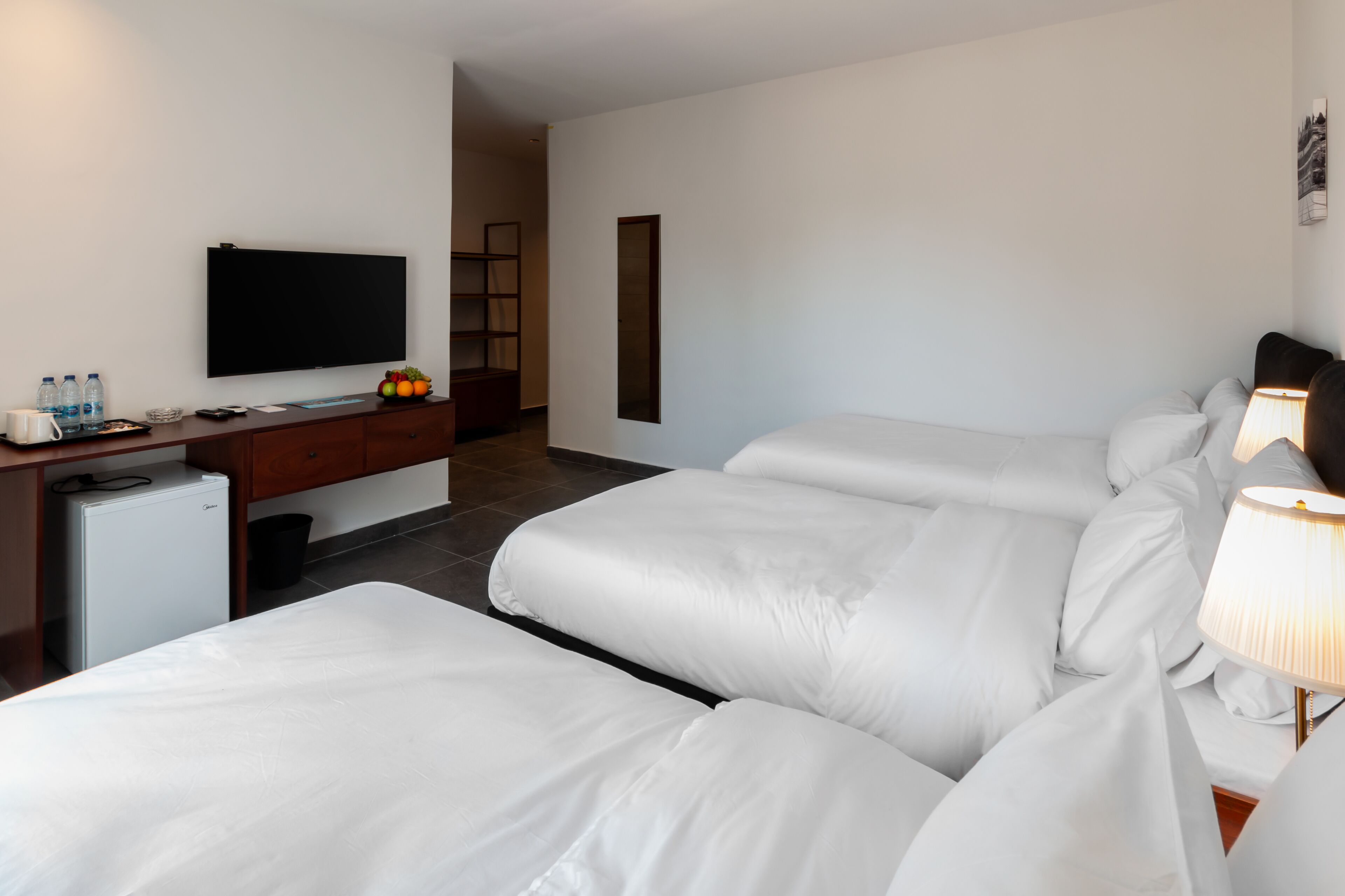 Une chambre d’hôtel avec deux lits, un bureau doté d’un téléviseur à écran plat, un mini-réfrigérateur et un panier de fruits.