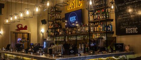 Zona de bar con temática rústica, que incluye un letrero de neón, estantes con botellas y un menú en la pizarra.