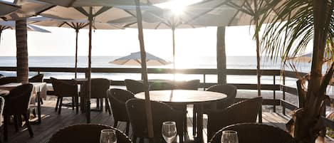 Un restaurante frente a la playa con mesas dispuestas para comer, con vista al océano.