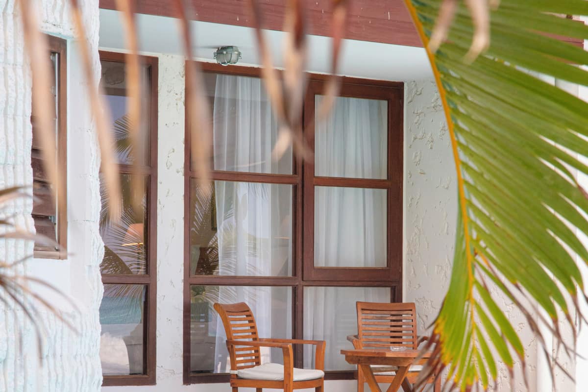 Zona de piscina con dos sillas y una mesa de madera, una ventana con cortinas y vista al estanque.
