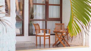 Zona de piscina con dos sillas y una mesa de madera, una ventana con cortinas y vista al estanque.