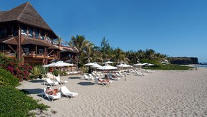 A beachfront hotel with a thatched roof, multiple lounge areas with umbrellas, and a view of the ocean. - Le Saint Alexis (Saint-Paul)
