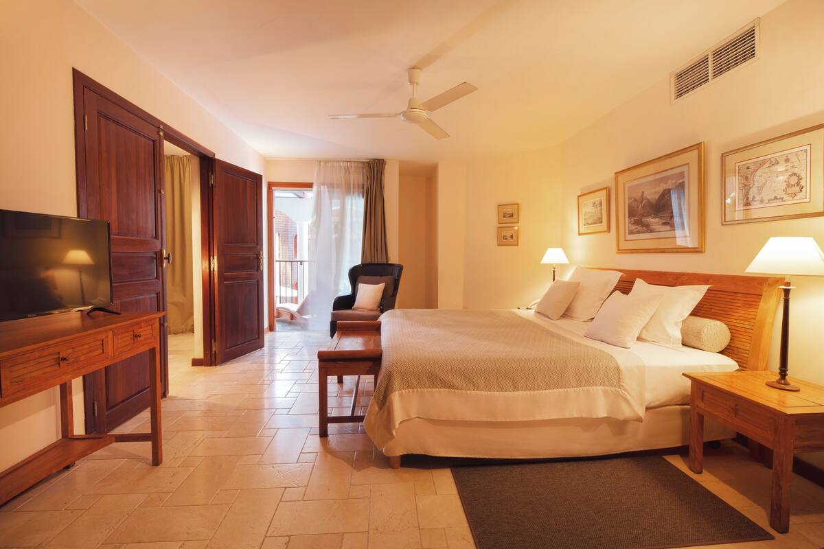 Una habitación de hotel con cama, mesita de noche, televisor, armario de madera y una silla.