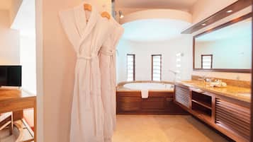 A modern bathroom with a large bathtub, a vanity with a mirror, and two white robes hanging on a rack.