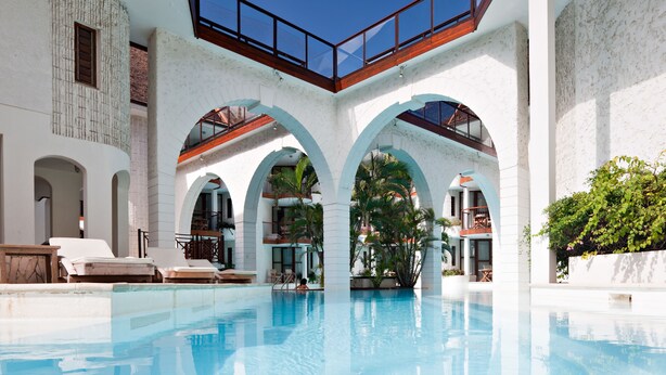 A pool area with clear blue water, white walls, and arches. There are lounge chairs and a staircase leading to upper levels. - Le Saint Alexis (Saint-Paul)