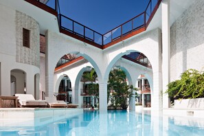 A pool area with clear blue water, white walls, and arches. There are lounge chairs and a staircase leading to upper levels. - Le Saint Alexis (Saint-Paul)