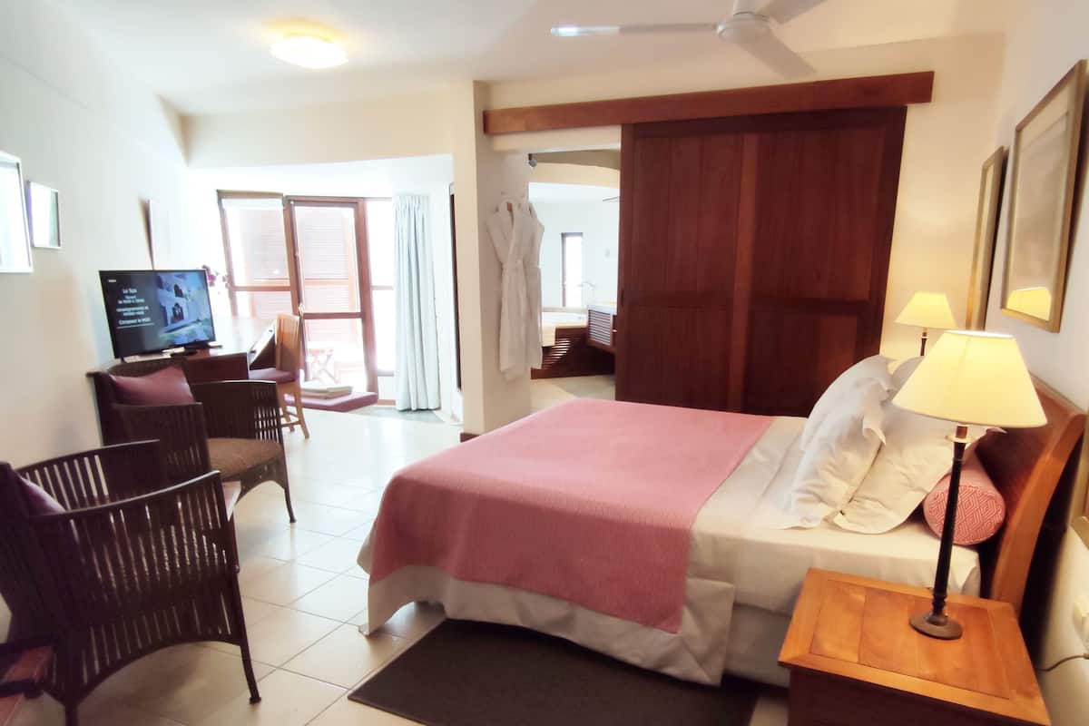 Habitación de hotel con cama, escritorio, silla, televisor y ventana con cortinas.