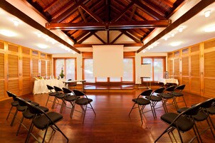 Un salón de conferencias con suelos de madera, techo alto con vigas a la vista y filas de sillas mirando hacia una mesa central.