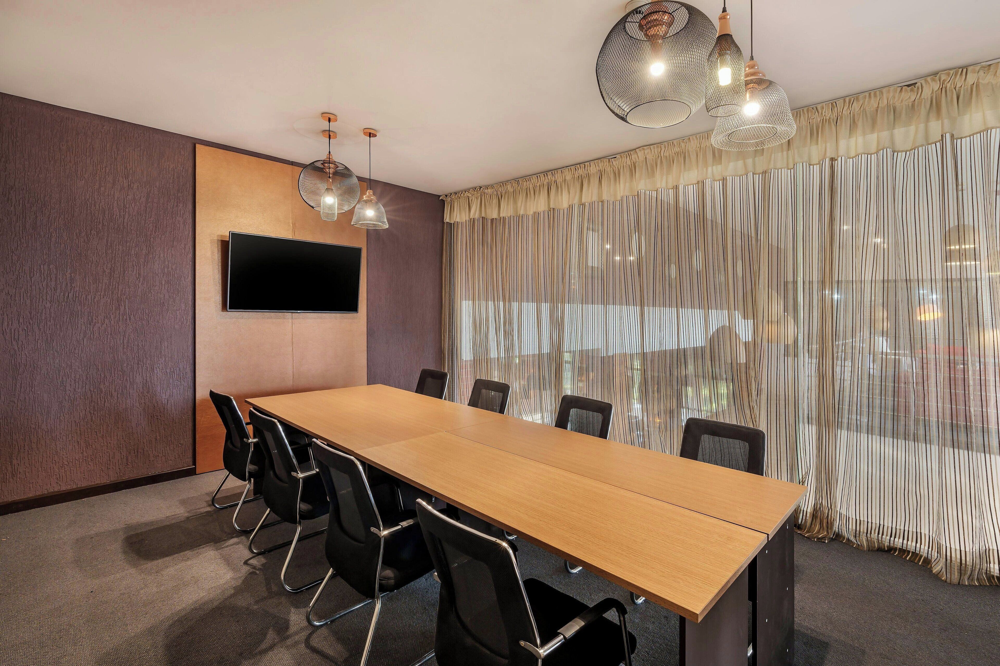 A conference room with a long table, black chairs, a flat-screen TV, and pendant lights.