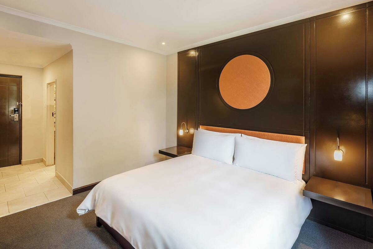 Une chambre d’hôtel avec un grand lit, un luminaire rond fixé au mur et une tête de lit en bois.