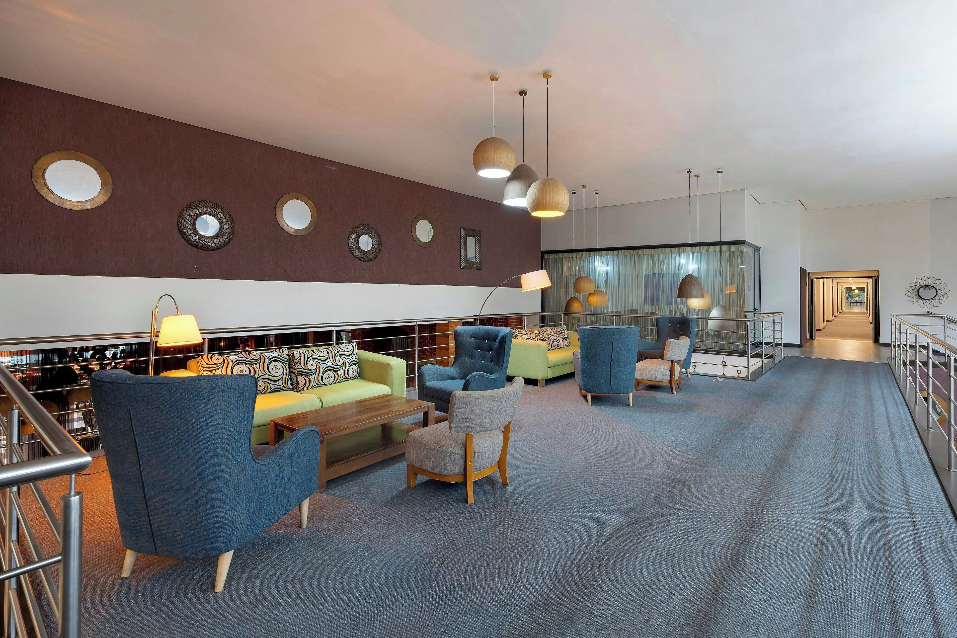 Eine moderne Lobby mit verschiedenen Sitzgelegenheiten, darunter Sessel und Sofas, sowie einer Treppe mit Metallgeländern.