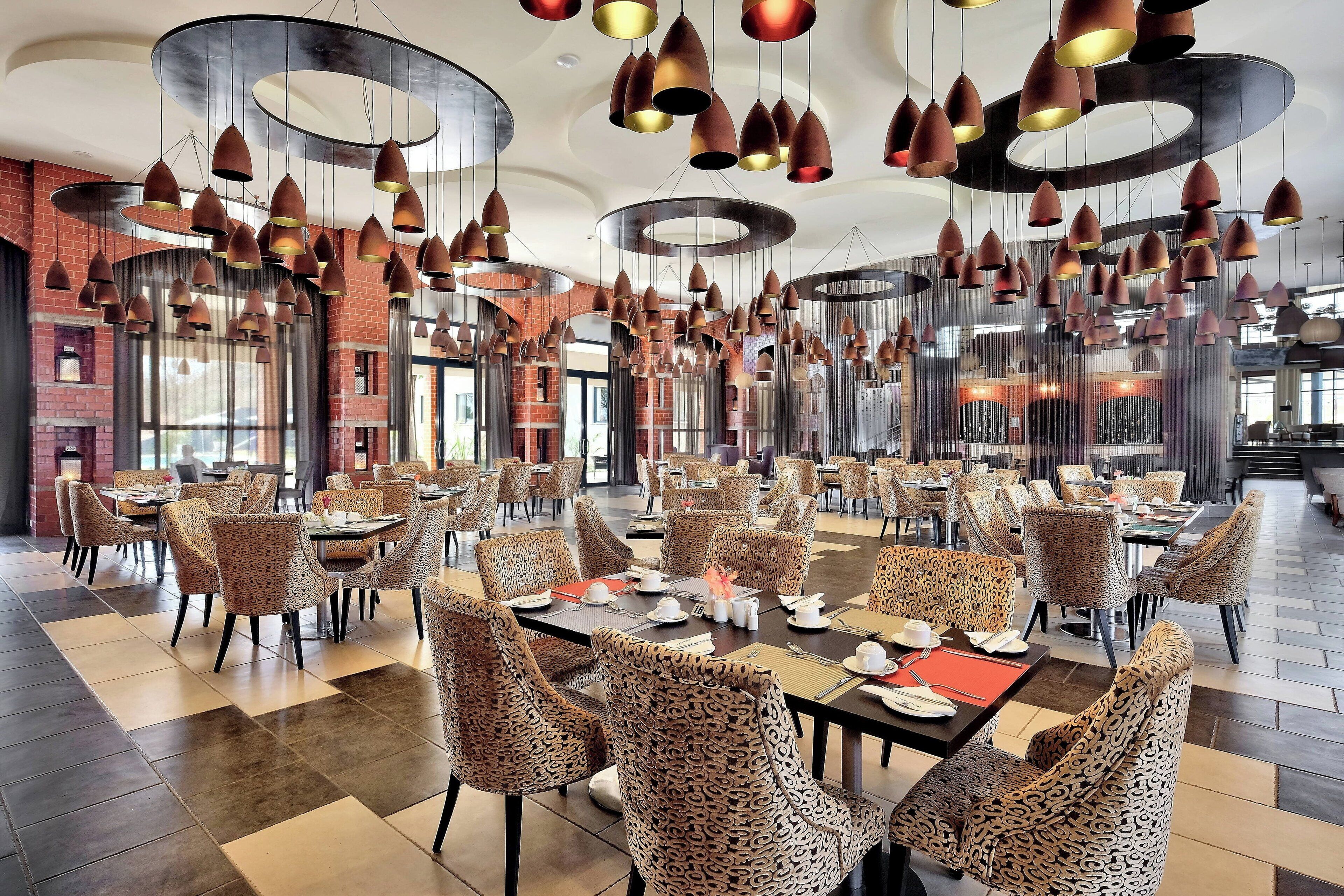 A spacious dining area with round tables and leopard-print chairs, featuring a modern ceiling design with hanging pendant lights.