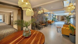 Un vestíbulo espacioso con mobiliario moderno, incluyendo una mesa redonda de madera, asientos cómodos e iluminación decorativa.