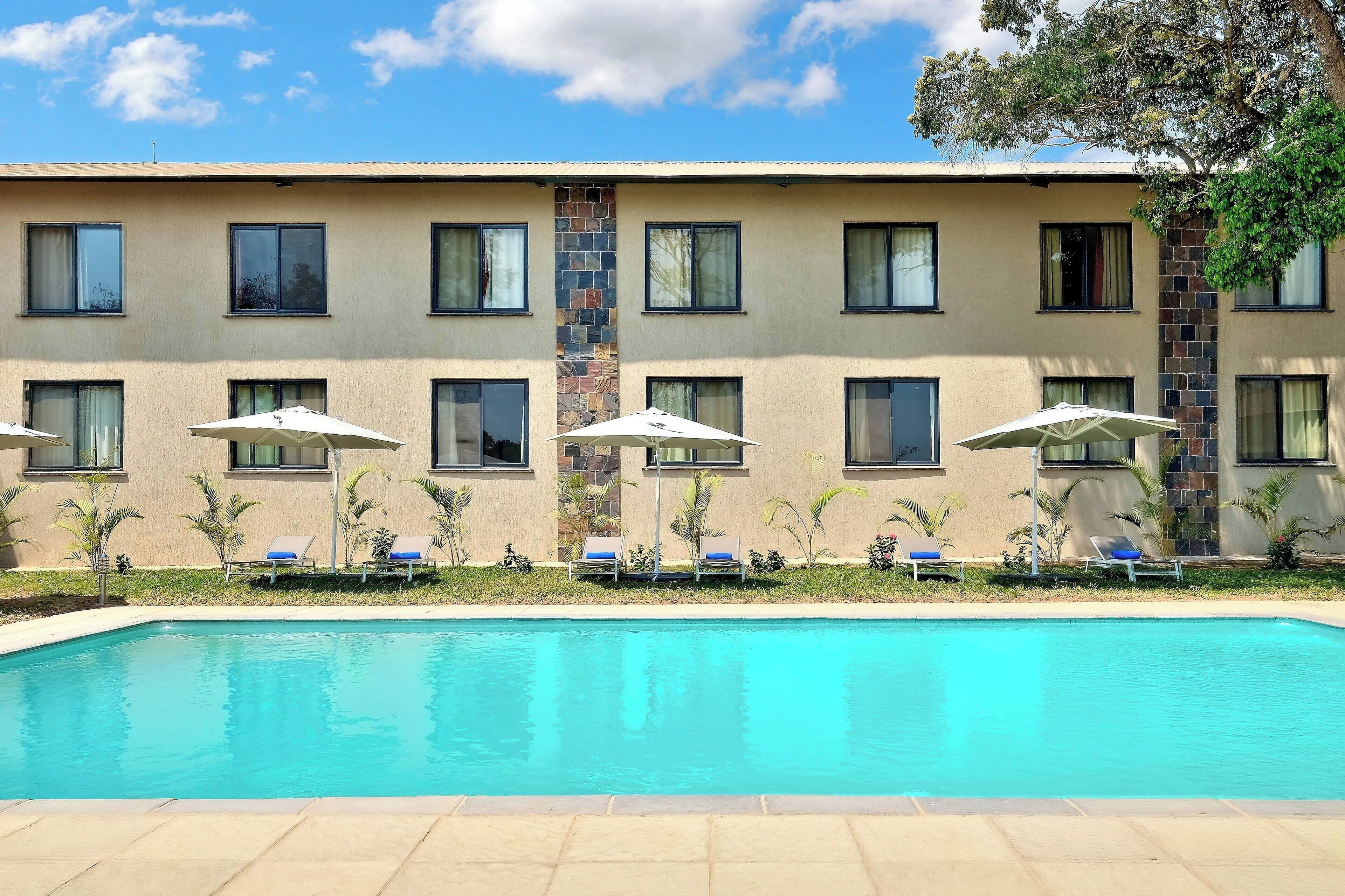 A hotel with a swimming pool, multiple windows, and outdoor seating with umbrellas.