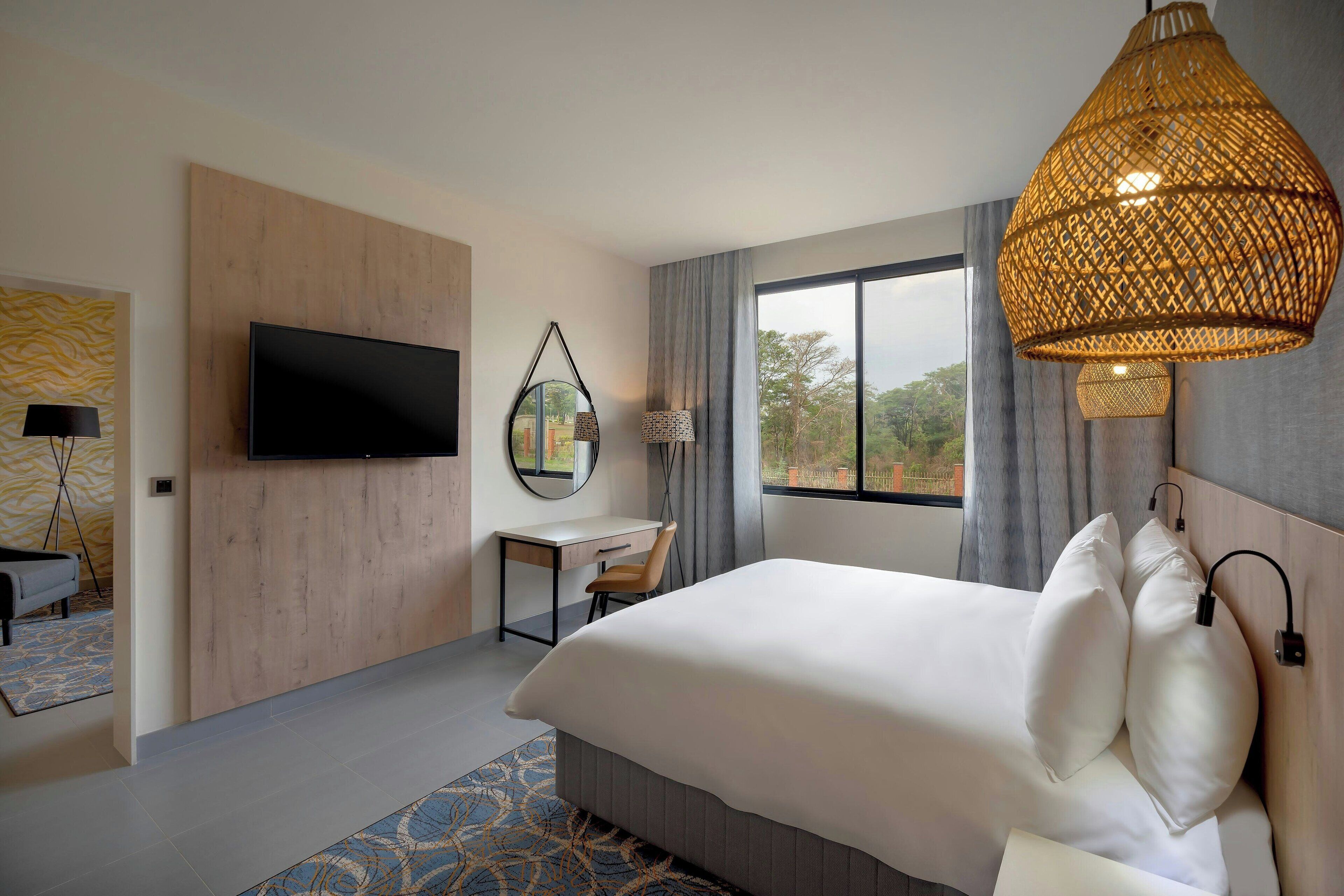 Quarto de hotel moderno com uma cama grande, uma mesa de escritório, televisão e uma janela ampla com vista.