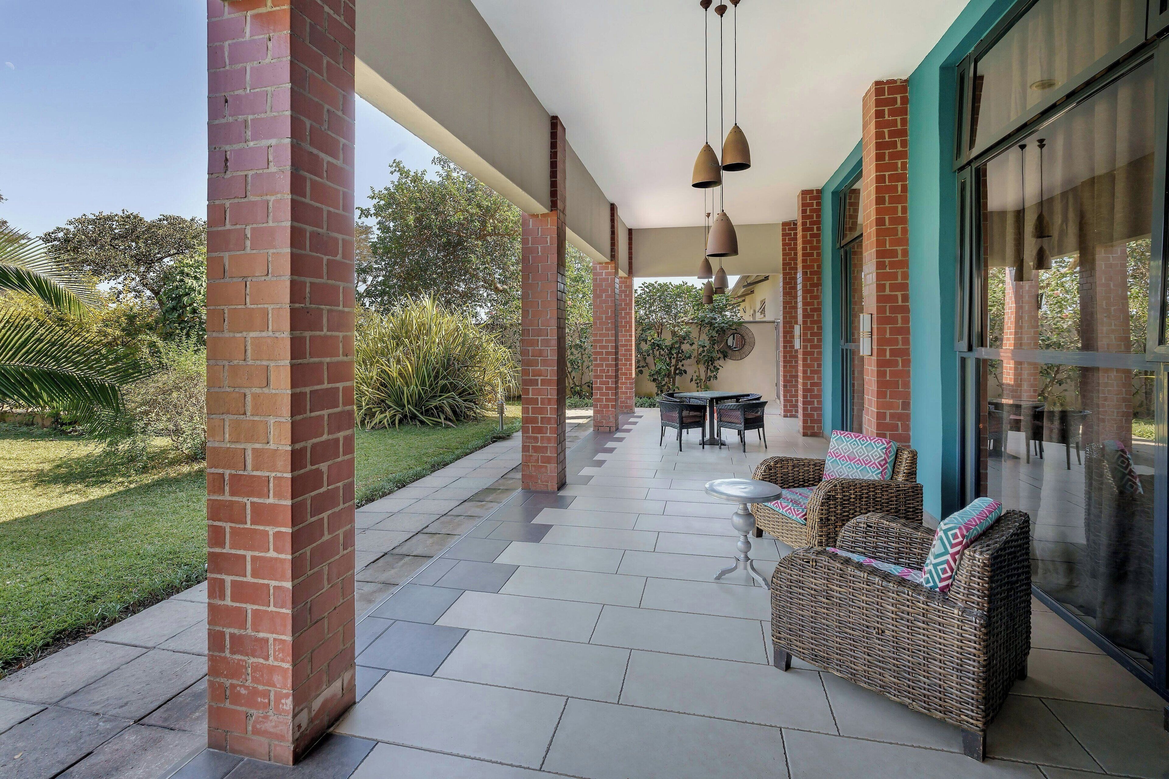 A covered patio with brick columns, outdoor furniture, and a glass door leading to a garden.