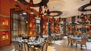 Un restaurante espacioso con numerosas mesas y sillas, ventanas amplias y lámparas colgantes.