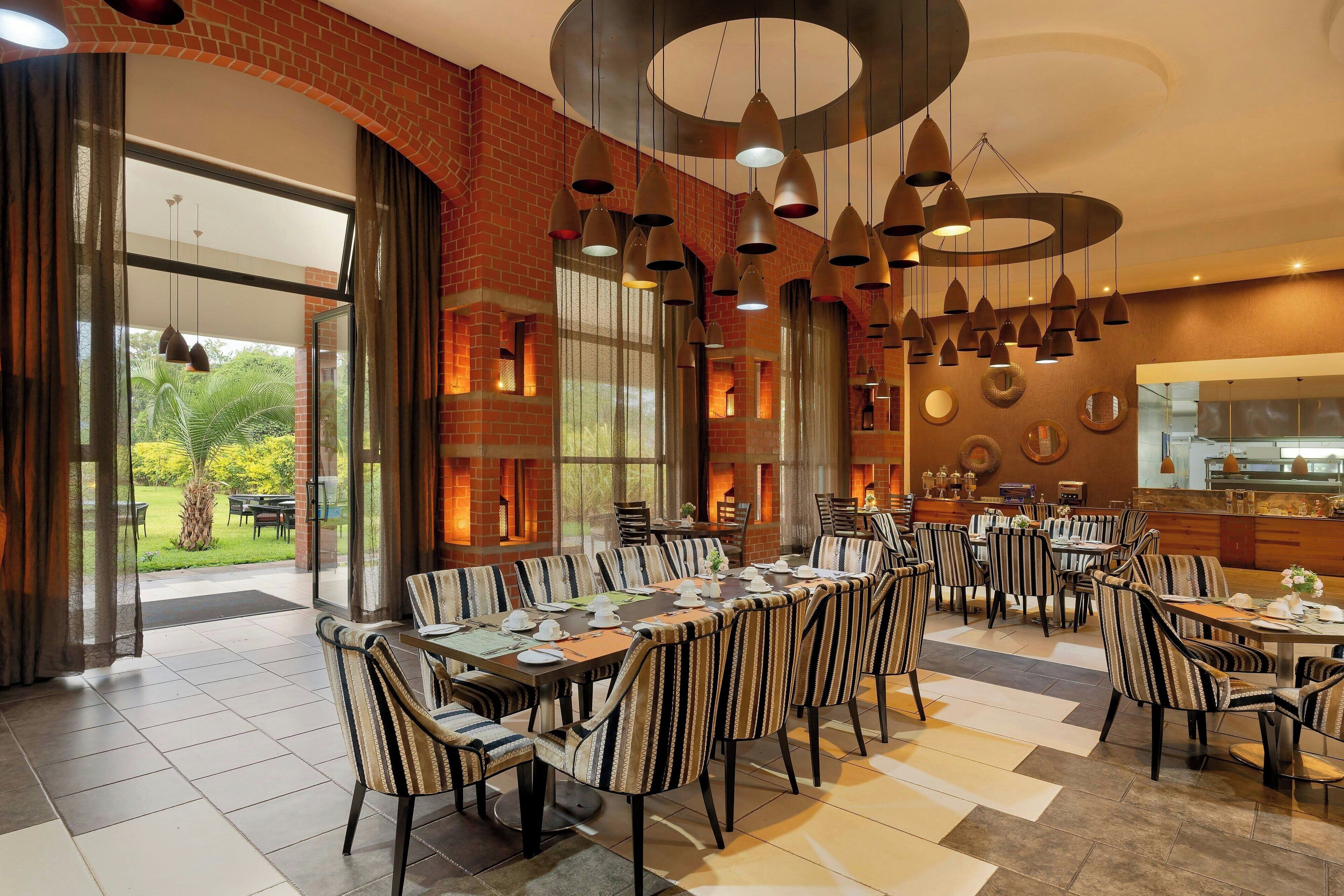 A spacious dining area with striped chairs and tables, large windows, and a brick wall.