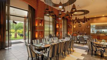 A spacious dining area with striped chairs and tables, large windows, and a brick wall.