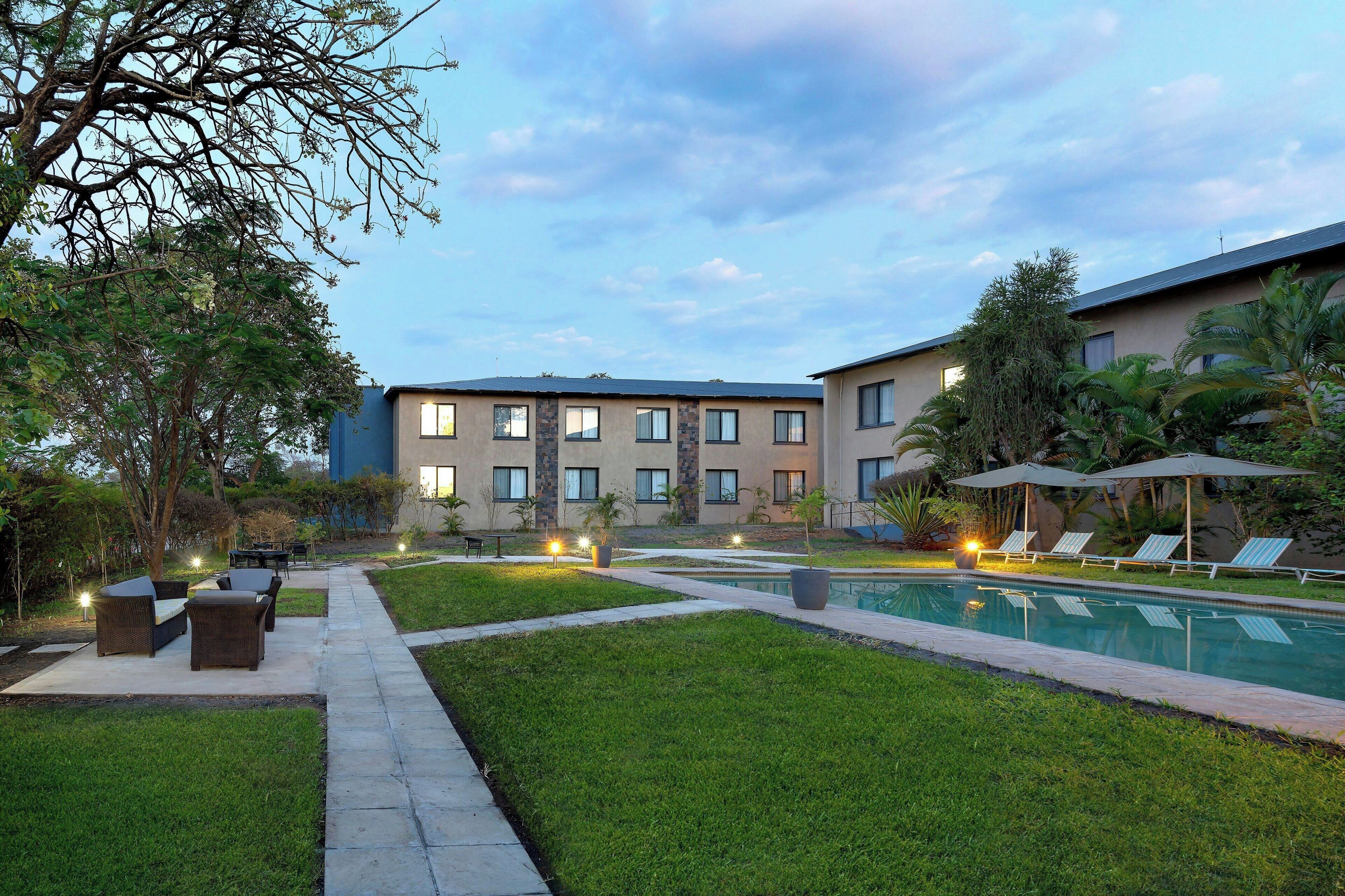 Un patio de hotel con piscina, mobiliario exterior y un césped bien cuidado.