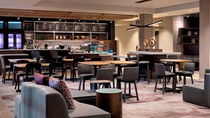 Un café moderno con diversas opciones de asientos, incluyendo mesas, sillas y sofás. Cuenta con una barra, un tablero de menú y una máquina de café.