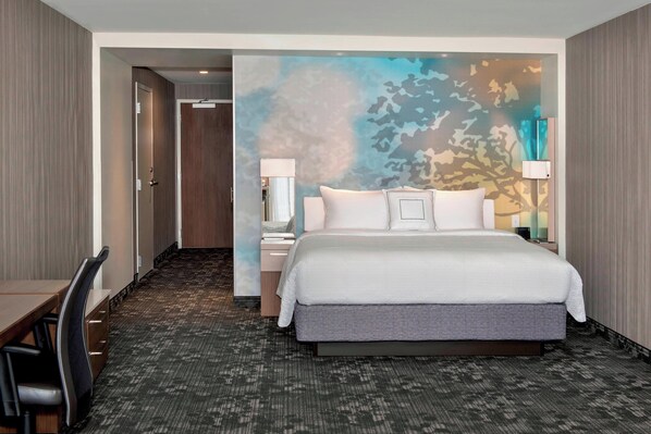 Habitación de hotel con una cama grande, dos mesitas de noche con lámparas, un escritorio con silla y suelo alfombrado.