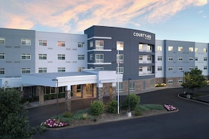 Um hotel Courtyard by Marriott com design moderno, vários andares e área de entrada coberta.