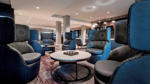 Un área de descanso moderna con sillones tapizados en azul, una mesa redonda en el centro y una alfombra estampada.