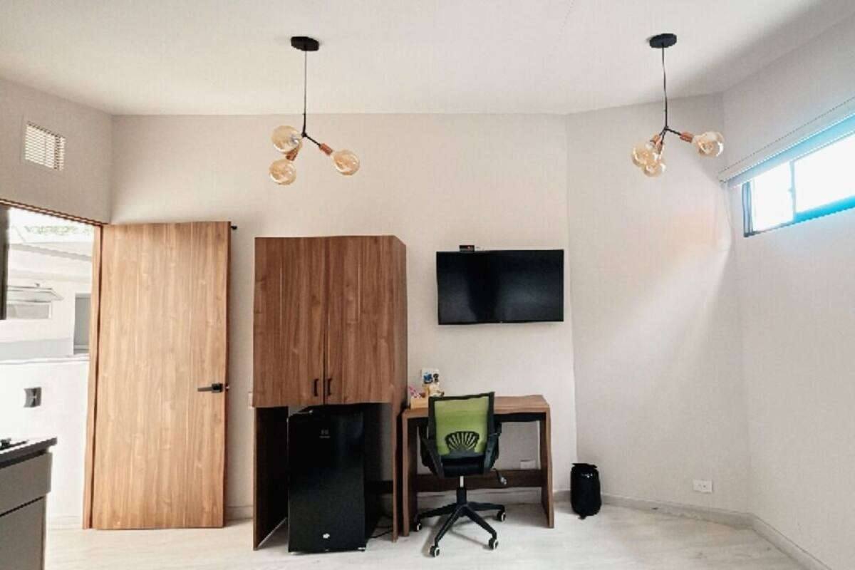 A modern office space with a wooden wardrobe, a desk with a chair, a black speaker, and a mounted TV.