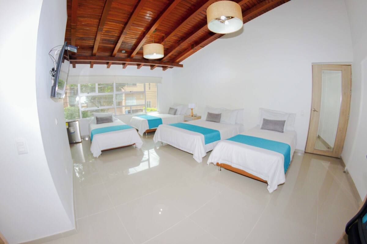 A hotel room with three beds, a wooden ceiling, and a large window.