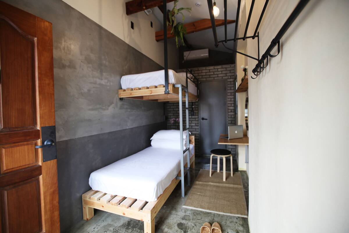 Una habitación pequeña con una cama individual superpuesta, un escritorio, una silla y una puerta.