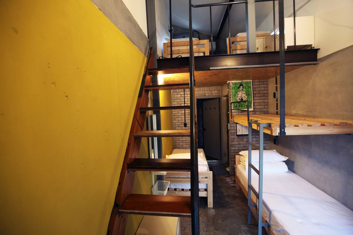 Habitación pequeña con literas, una escalera y una pared de ladrillo.