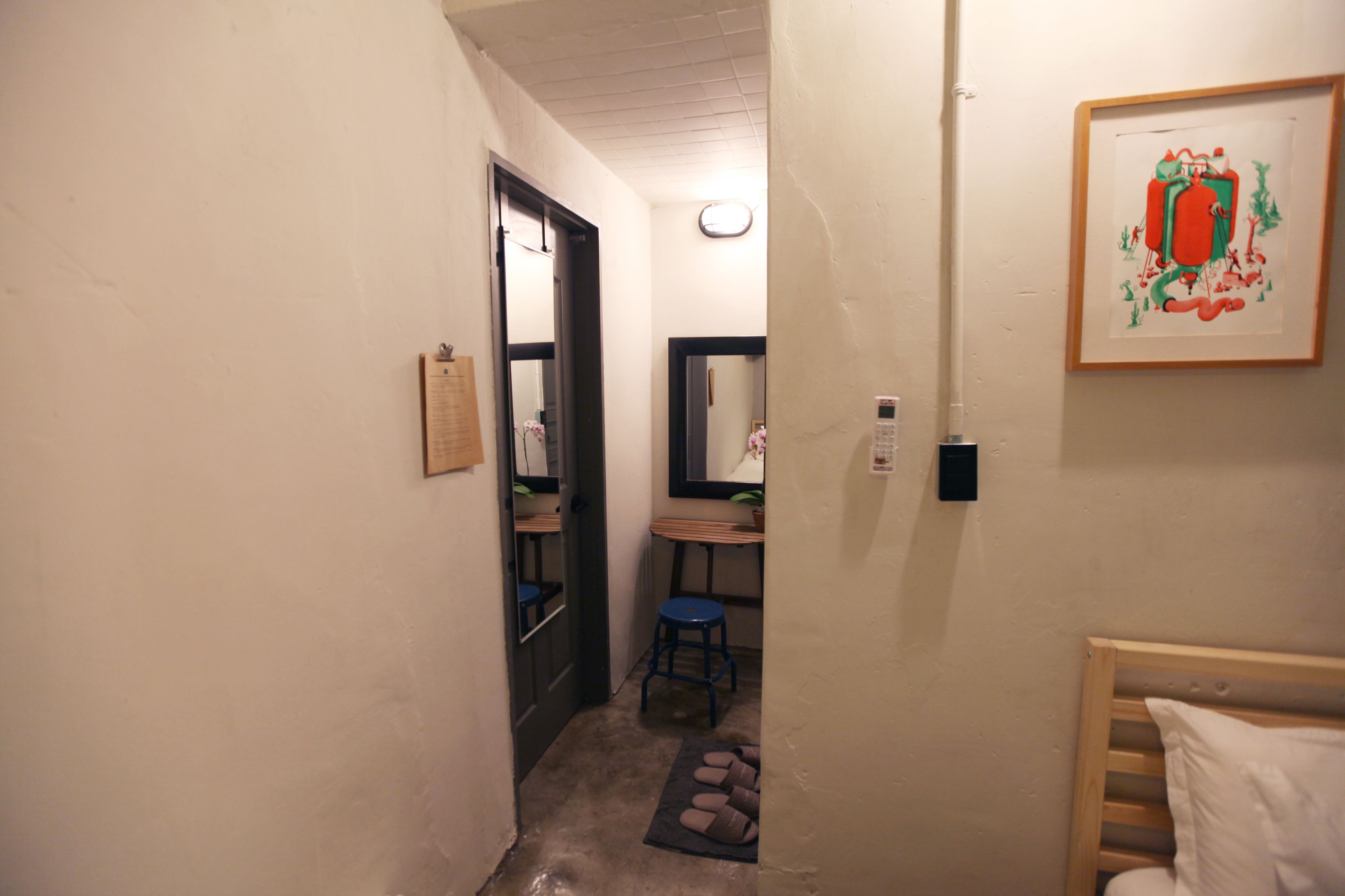 A narrow hallway with a wooden door, a blue stool, a small table, and a framed picture on the wall.
