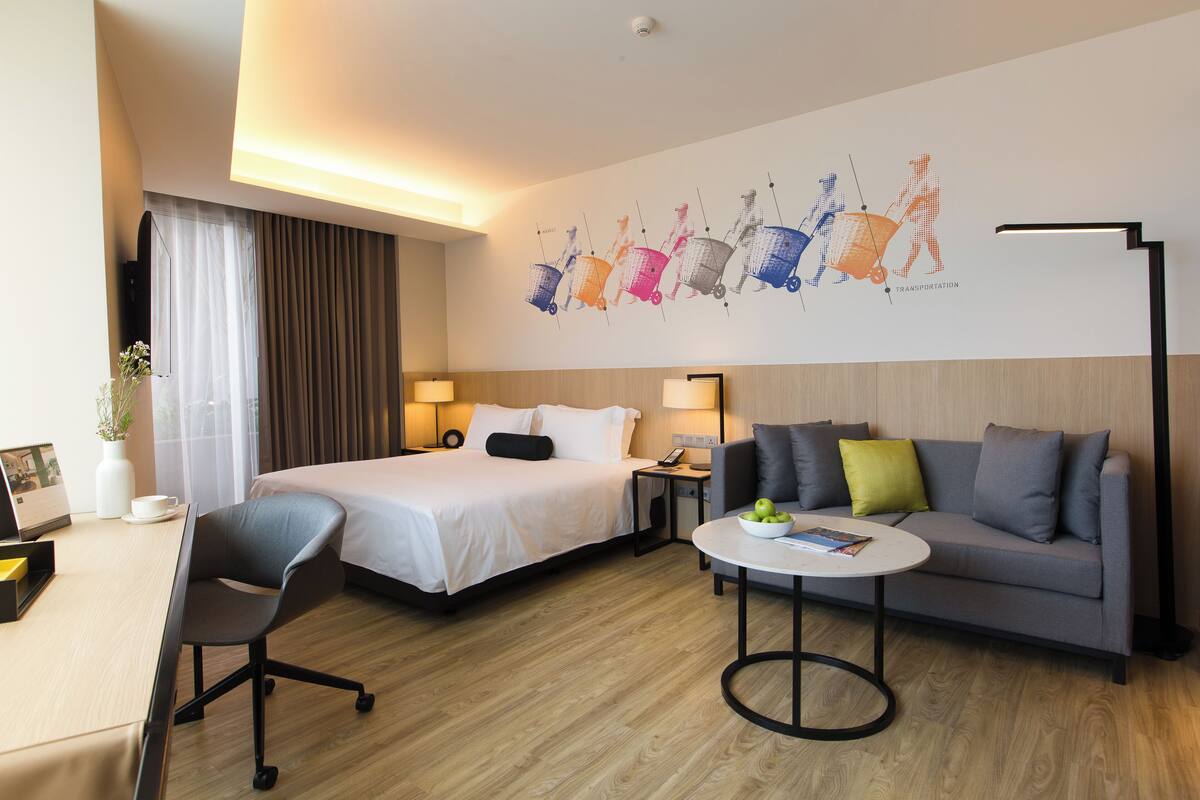 Quarto de hotel com cama, sofá, escrivaninha e luminária.