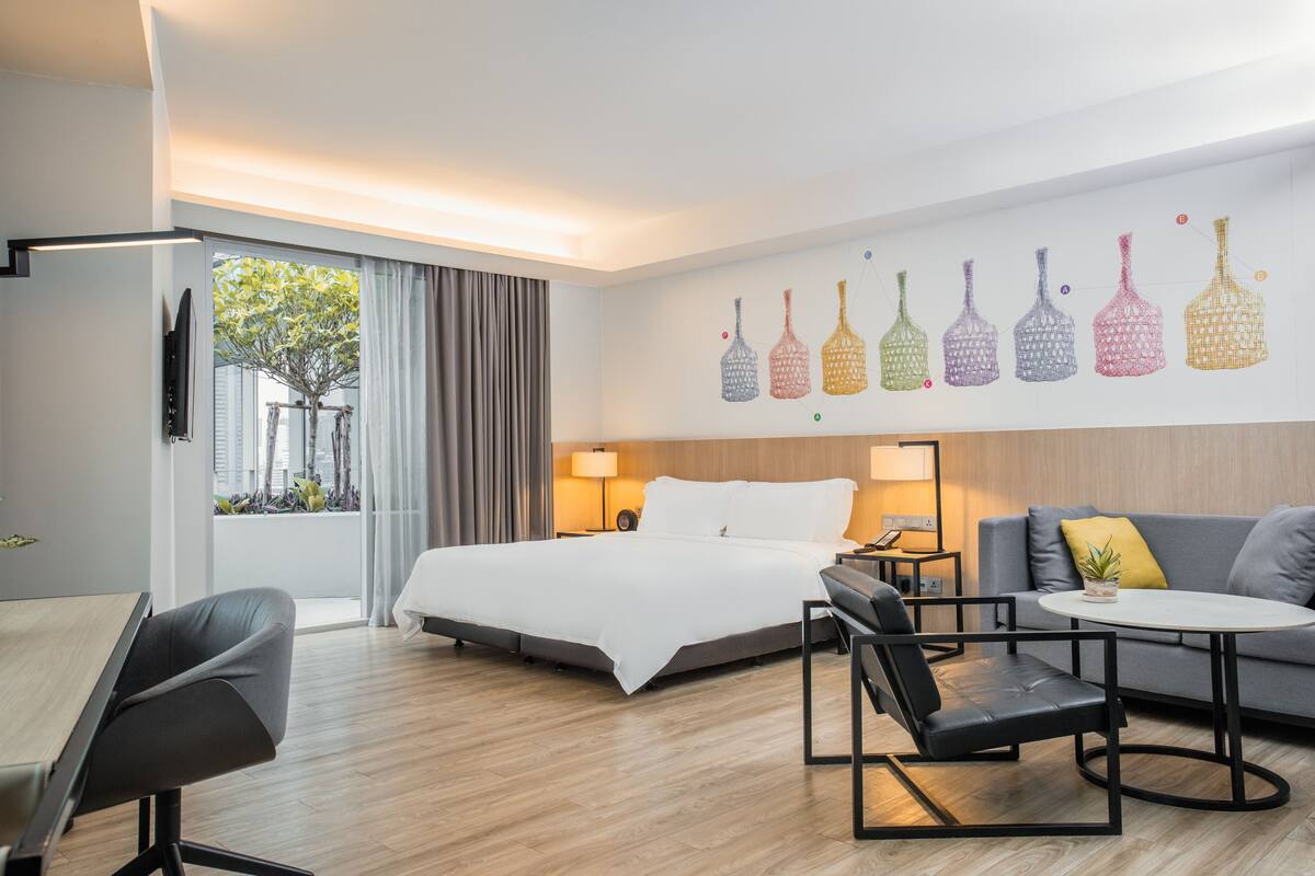 Quarto de hotel moderno com uma cama grande, um sofá, uma mesa de jantar e uma televisão.