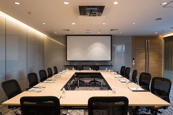 Une salle de conférence avec une longue table, des chaises, un écran de projection et une grande fenêtre.
