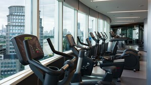 A modern gym with various exercise machines and large windows offering a city view. - Modena by Fraser Bangkok Hotel Residences (Bangkok)