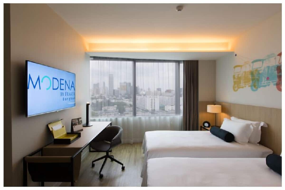 A hotel room with a bed, a desk, a chair, a TV, and a city view.